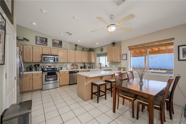 kitchen with appliances with stainless steel finishes, light brown cabinets, light countertops, and a kitchen breakfast bar