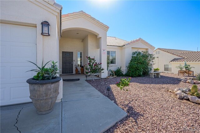 property entrance featuring a tile roof, an attached garage, and stucco siding