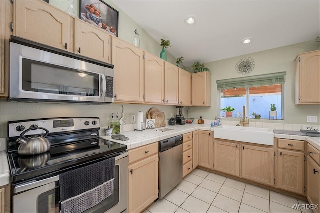 kitchen with light tile patterned floors, stainless steel appliances, tile counters, light brown cabinetry, and a sink