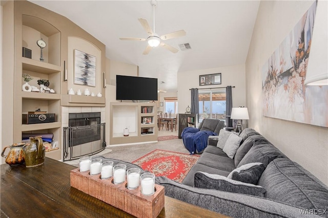 living room with visible vents, built in features, a tile fireplace, ceiling fan, and carpet