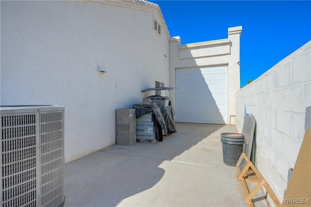 view of patio / terrace featuring concrete driveway, central AC, fence, and an attached garage