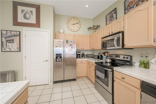 kitchen with tile countertops, light brown cabinetry, appliances with stainless steel finishes, and light tile patterned floors