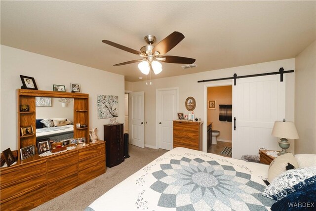 carpeted bedroom with ensuite bath, a barn door, visible vents, and ceiling fan