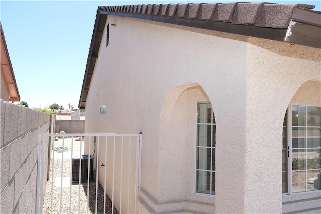view of side of home featuring stucco siding, fence, and central AC unit
