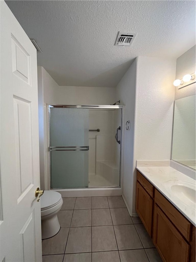 bathroom featuring a stall shower, toilet, a textured ceiling, tile patterned flooring, and vanity
