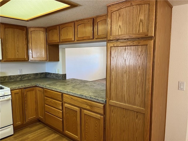 kitchen with white range with electric stovetop, brown cabinets, light wood finished floors, and dark countertops