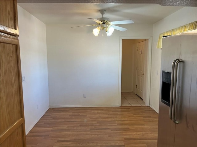 unfurnished dining area featuring light wood-type flooring, a ceiling fan, and baseboards
