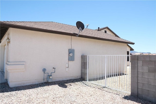 view of home's exterior with fence, stucco siding, a gate, and a shingled roof