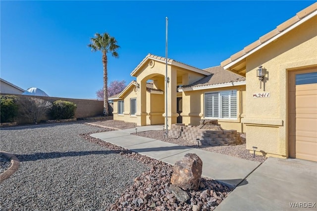 exterior space featuring an attached garage, fence, and stucco siding