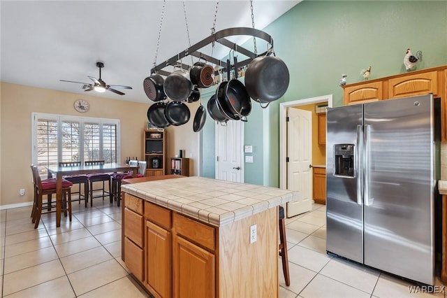 kitchen featuring stainless steel fridge with ice dispenser, tile countertops, ceiling fan, a kitchen island, and light tile patterned flooring