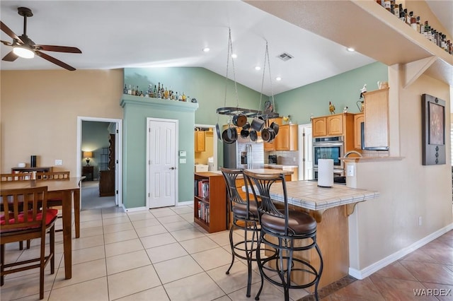 kitchen with light tile patterned floors, stainless steel double oven, a breakfast bar area, a peninsula, and tile counters