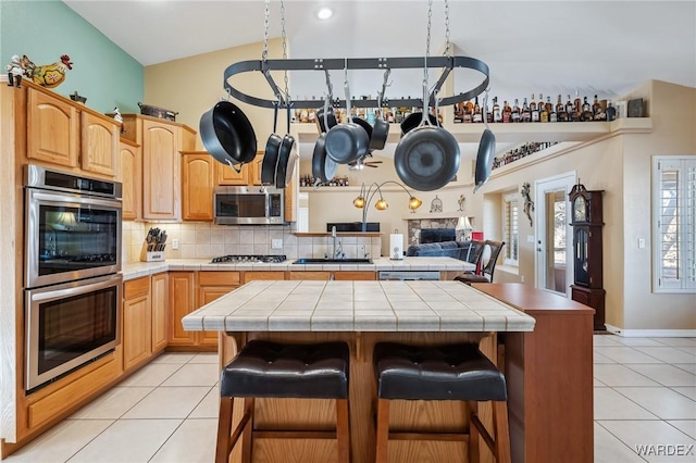 kitchen with light tile patterned flooring, stainless steel appliances, a sink, tile counters, and a center island