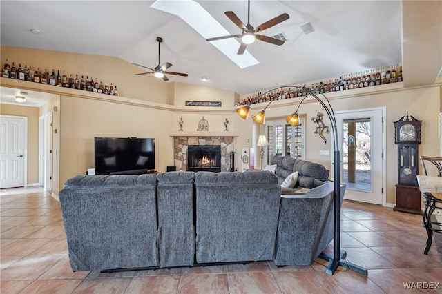 living room with baseboards, lofted ceiling with skylight, ceiling fan, a fireplace, and light tile patterned flooring