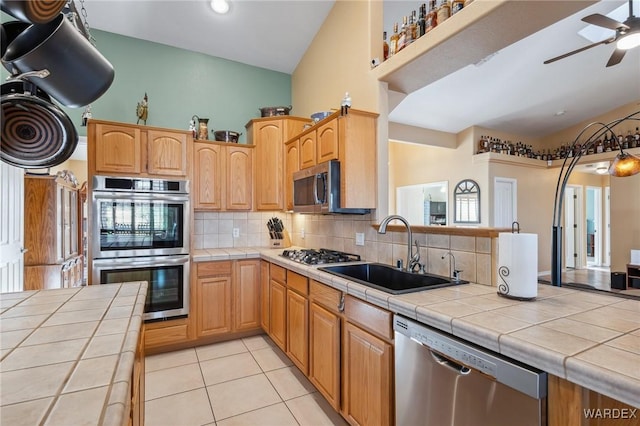 kitchen with light tile patterned flooring, stainless steel appliances, a sink, tile counters, and decorative backsplash