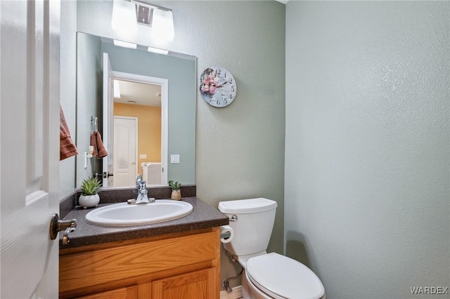 half bath featuring a textured wall, vanity, and toilet