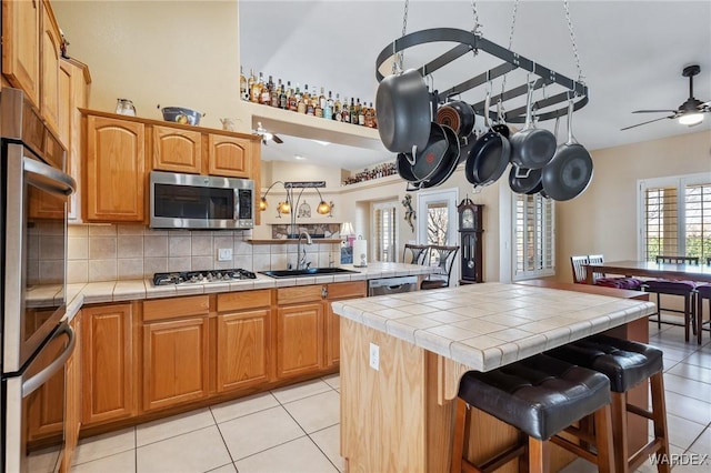 kitchen featuring appliances with stainless steel finishes, a sink, tile countertops, and a ceiling fan