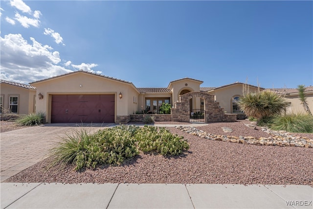 mediterranean / spanish-style home featuring a garage, a tile roof, stone siding, decorative driveway, and stucco siding