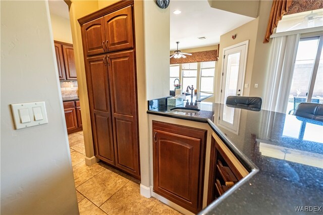 kitchen with light tile patterned floors, a sink, backsplash, brown cabinets, and dark stone counters