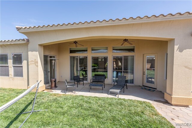 rear view of property featuring a patio area, ceiling fan, a lawn, and stucco siding