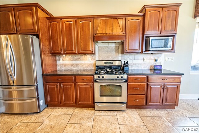 kitchen with light tile patterned flooring, baseboards, appliances with stainless steel finishes, backsplash, and custom range hood