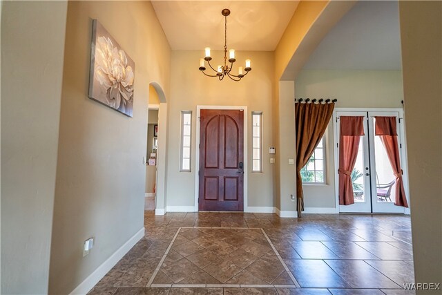 entryway featuring baseboards, arched walkways, an inviting chandelier, stone finish flooring, and french doors