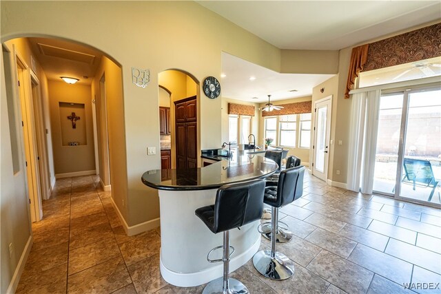 kitchen with baseboards, arched walkways, dark countertops, a kitchen breakfast bar, and a peninsula