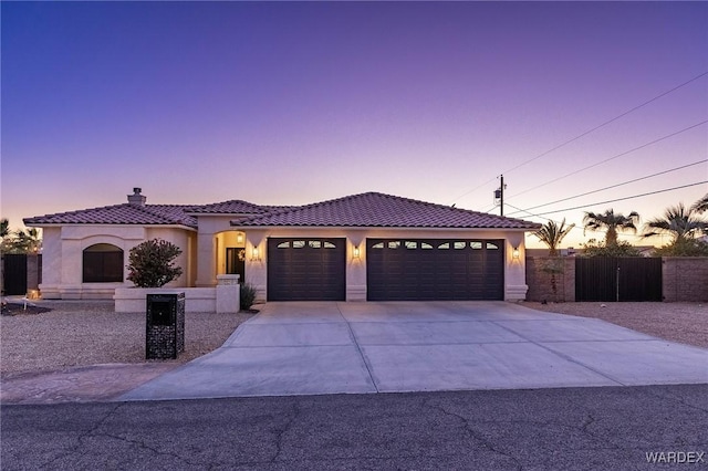 mediterranean / spanish-style home with a tiled roof, concrete driveway, an attached garage, and stucco siding