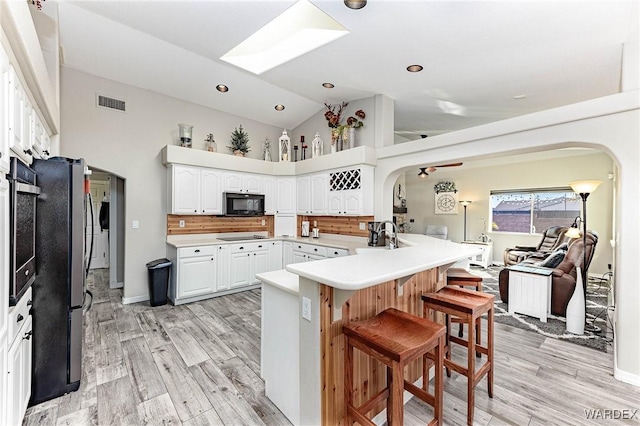 kitchen featuring open floor plan, a peninsula, light countertops, black appliances, and white cabinetry