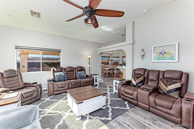 living room featuring arched walkways, light wood-style flooring, visible vents, and a ceiling fan