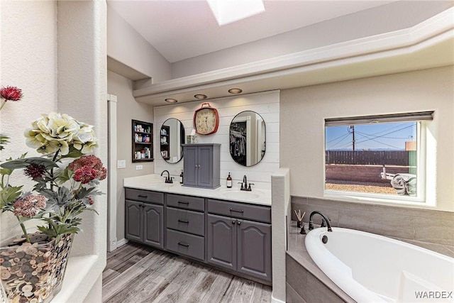 bathroom with double vanity, a garden tub, a sink, and wood finished floors