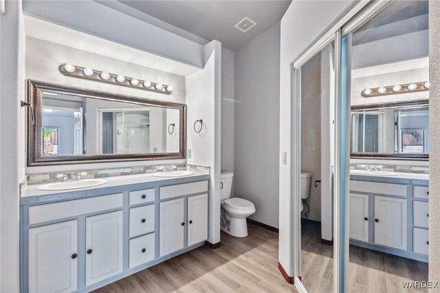 bathroom with double vanity, visible vents, toilet, wood finished floors, and a sink