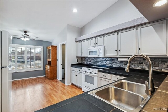 kitchen featuring white appliances, lofted ceiling, a sink, light wood-type flooring, and backsplash