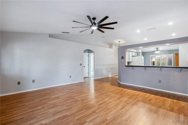 unfurnished living room with arched walkways, lofted ceiling, a ceiling fan, light wood-style floors, and baseboards