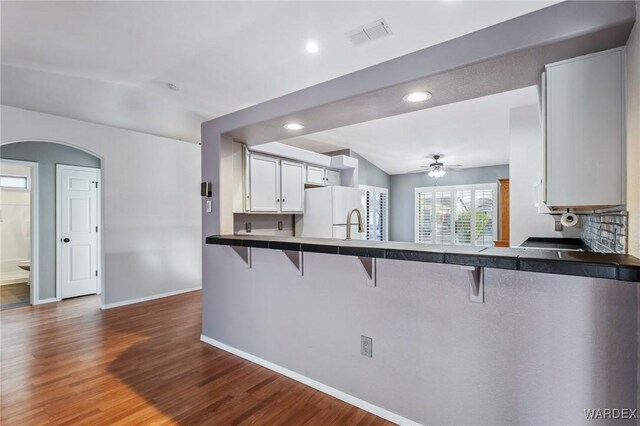 kitchen with dark countertops, freestanding refrigerator, white cabinets, a peninsula, and a kitchen bar