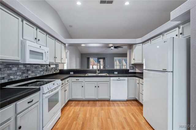 kitchen with white appliances, light wood finished floors, a ceiling fan, dark countertops, and a sink