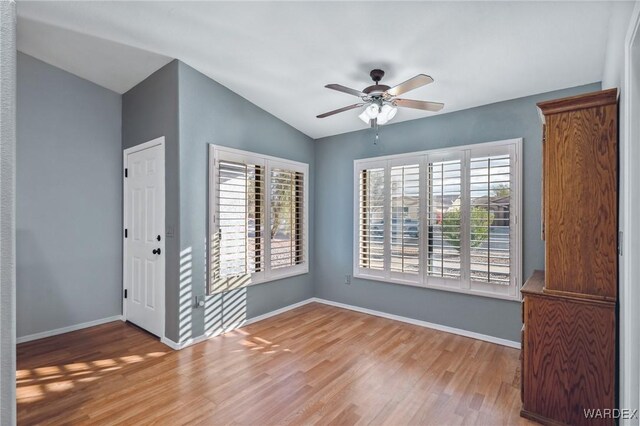 unfurnished room with lofted ceiling, a healthy amount of sunlight, a ceiling fan, and wood finished floors