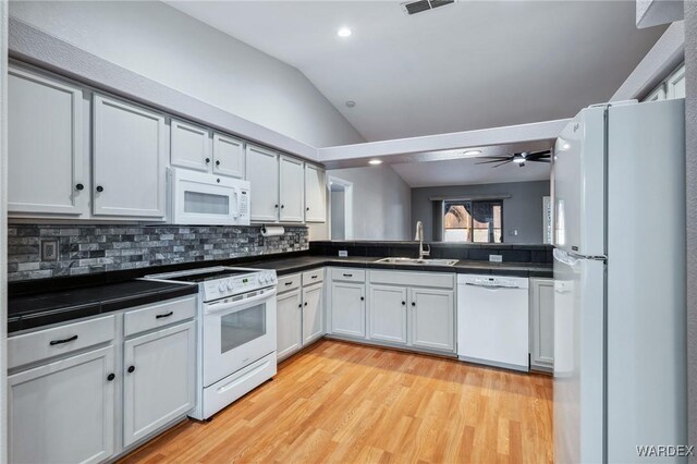 kitchen featuring white appliances, a sink, white cabinetry, vaulted ceiling, and dark countertops