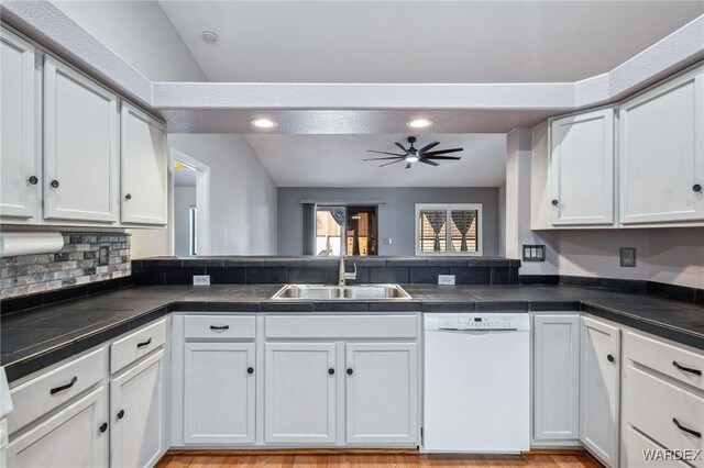 kitchen with dark countertops, white cabinets, white dishwasher, and a sink