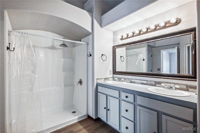 full bath featuring double vanity, a stall shower, a sink, and wood finished floors