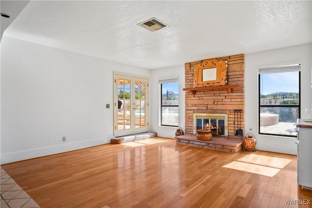 unfurnished living room featuring french doors, visible vents, a stone fireplace, a textured ceiling, and wood finished floors