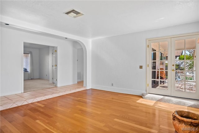 empty room featuring arched walkways, french doors, wood finished floors, and visible vents