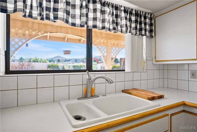 kitchen featuring light countertops, a sink, backsplash, and white cabinetry