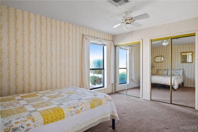 bedroom featuring multiple closets, visible vents, carpet flooring, and wallpapered walls