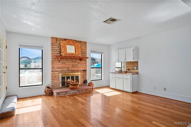 unfurnished living room with a fireplace, a sink, visible vents, baseboards, and light wood-type flooring