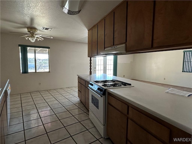 kitchen featuring light countertops, visible vents, white range with gas cooktop, a textured ceiling, and under cabinet range hood