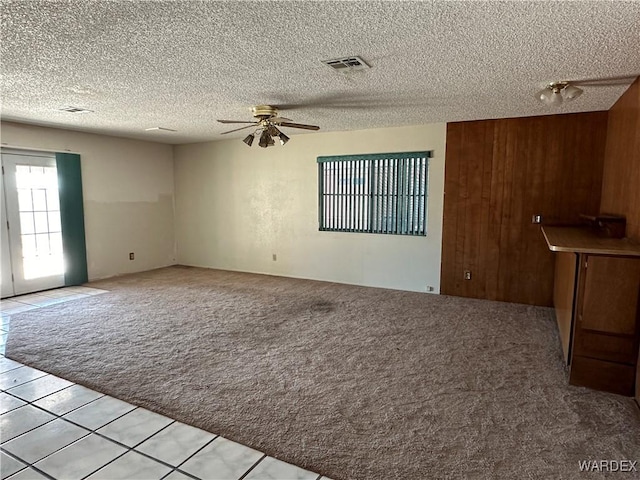 spare room featuring visible vents, light carpet, ceiling fan, wooden walls, and a textured ceiling