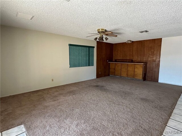 unfurnished living room with a ceiling fan, light colored carpet, visible vents, and wood walls