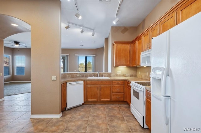 kitchen featuring arched walkways, brown cabinets, light countertops, a sink, and white appliances