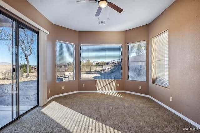 empty room featuring a ceiling fan, visible vents, a wealth of natural light, and carpet flooring