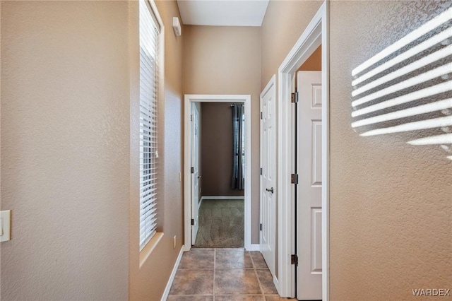 hall featuring tile patterned flooring, a textured wall, and baseboards